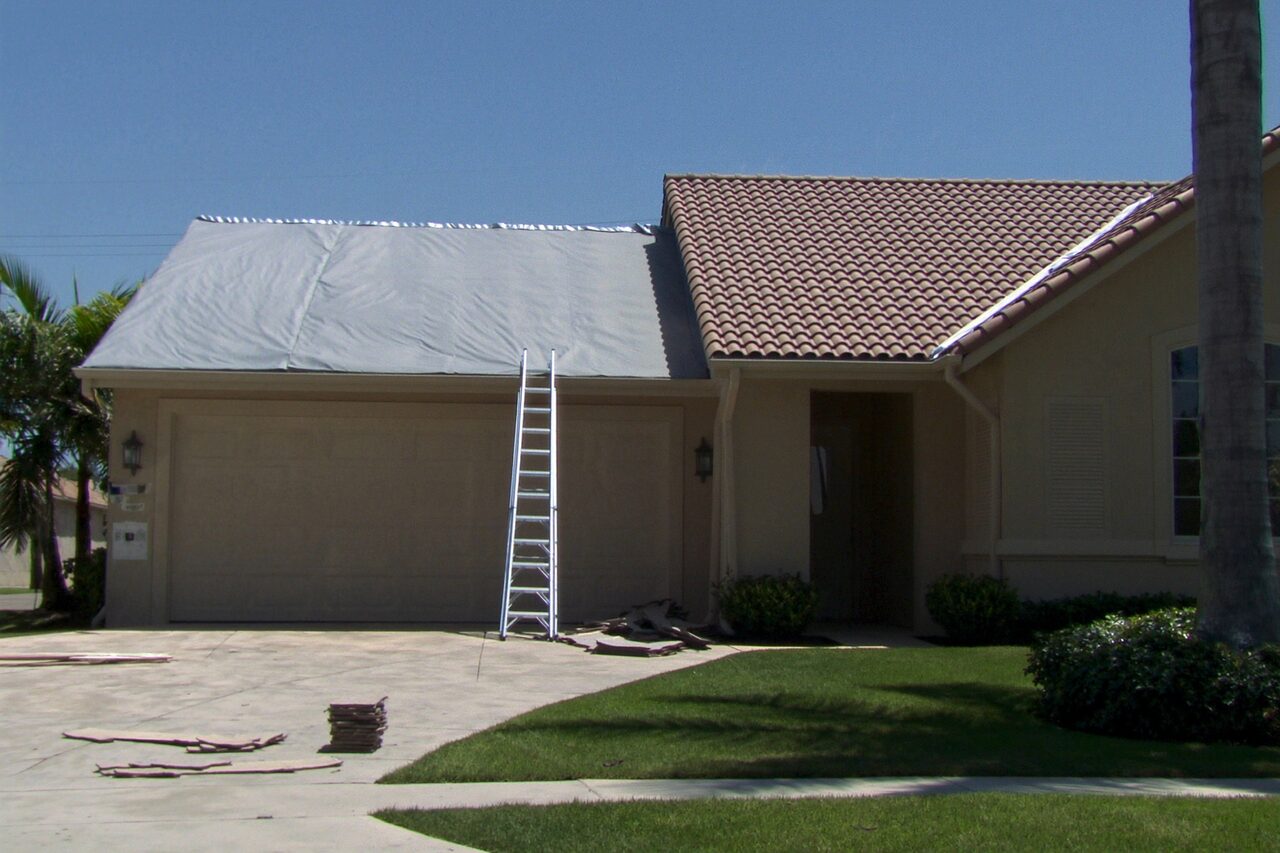 Single-story home mid re-roof with a ladder and protective covering over the roof deck