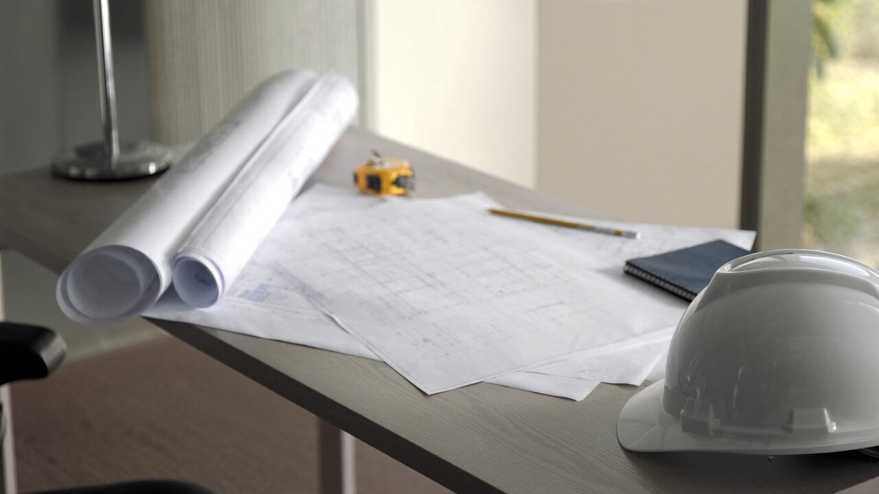 Rolled architectural blueprints, a tape measure and a hard hat on a desk